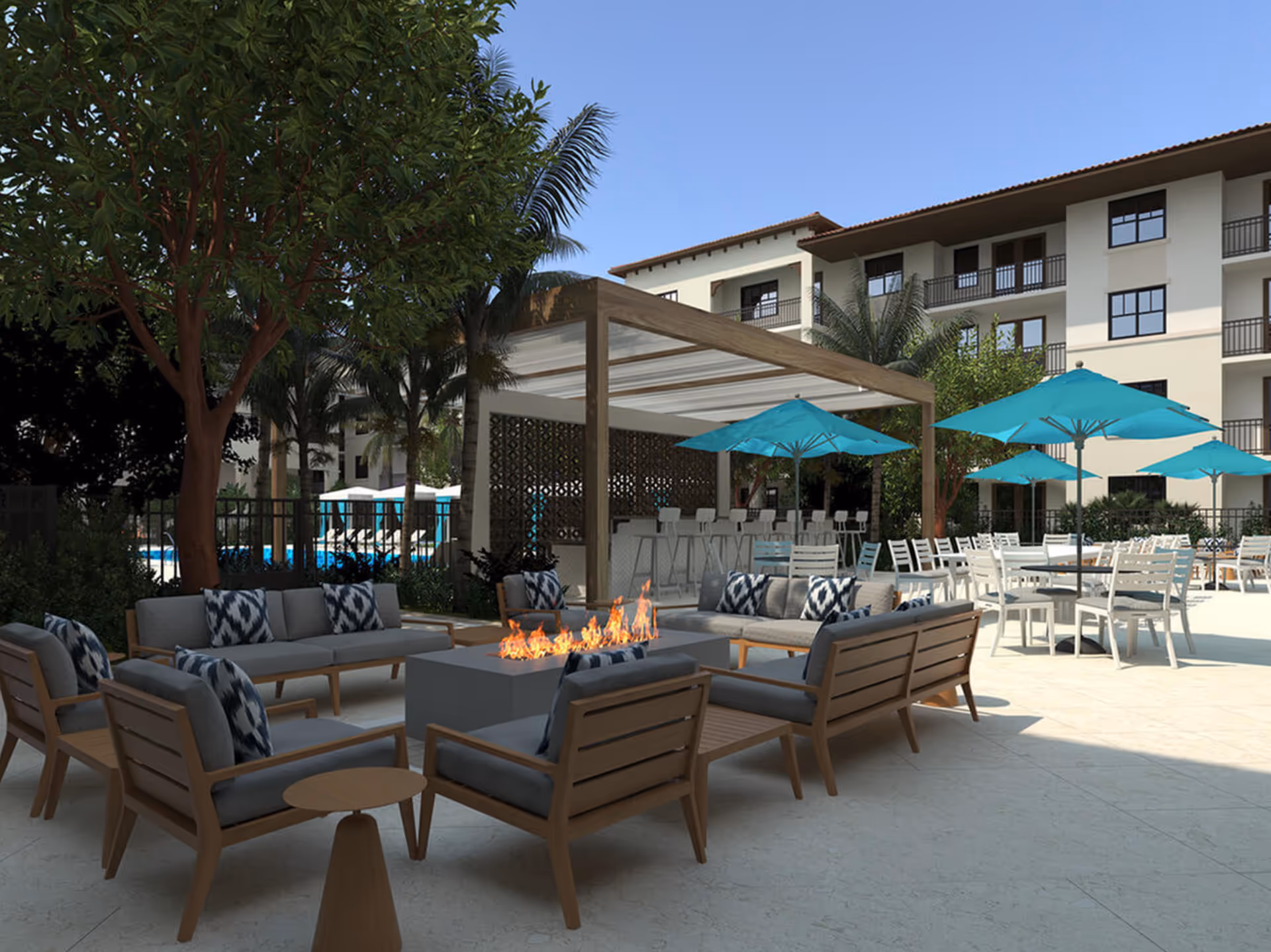 Outdoor courtyard with lounge seating around a fire pit, dining tables with teal umbrellas, and a multi-story building in the background.