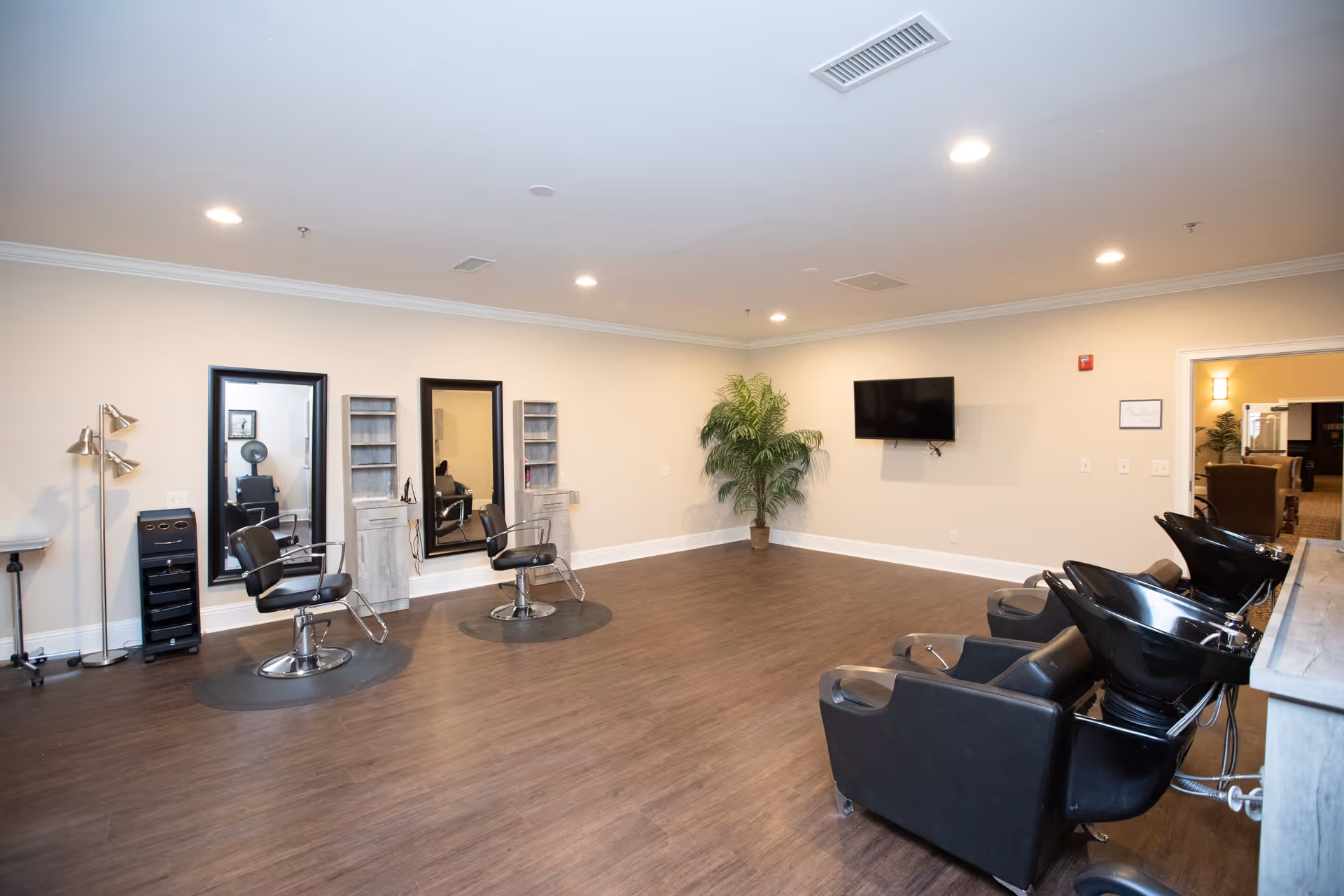 Spacious salon area with styling chairs and mirrors on the left and hair-washing stations on the right, plus a wall-mounted TV.