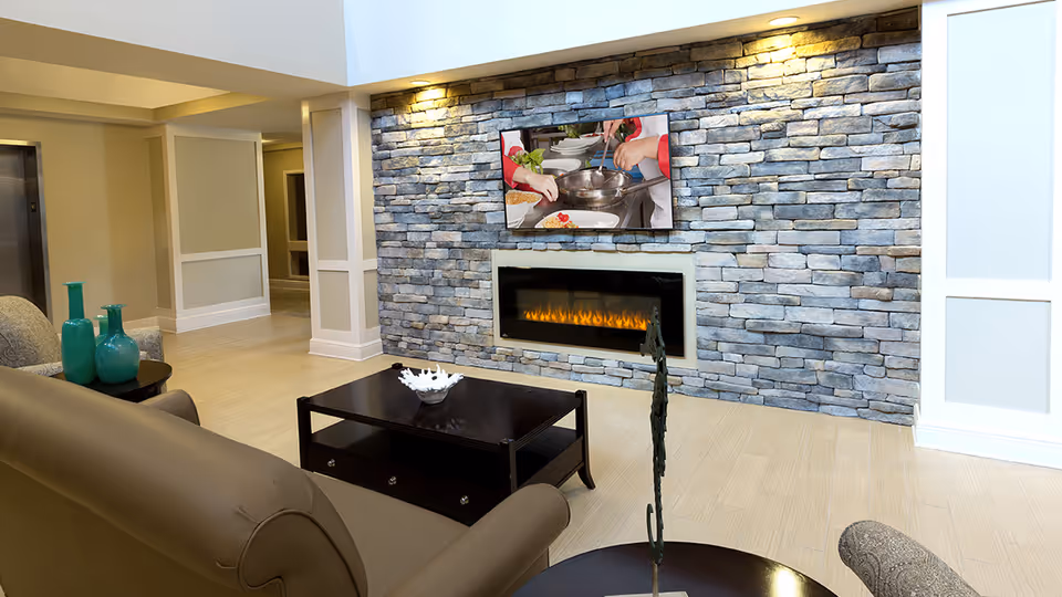 Modern lounge area with a stone fireplace, wall-mounted TV, coffee table and seating.