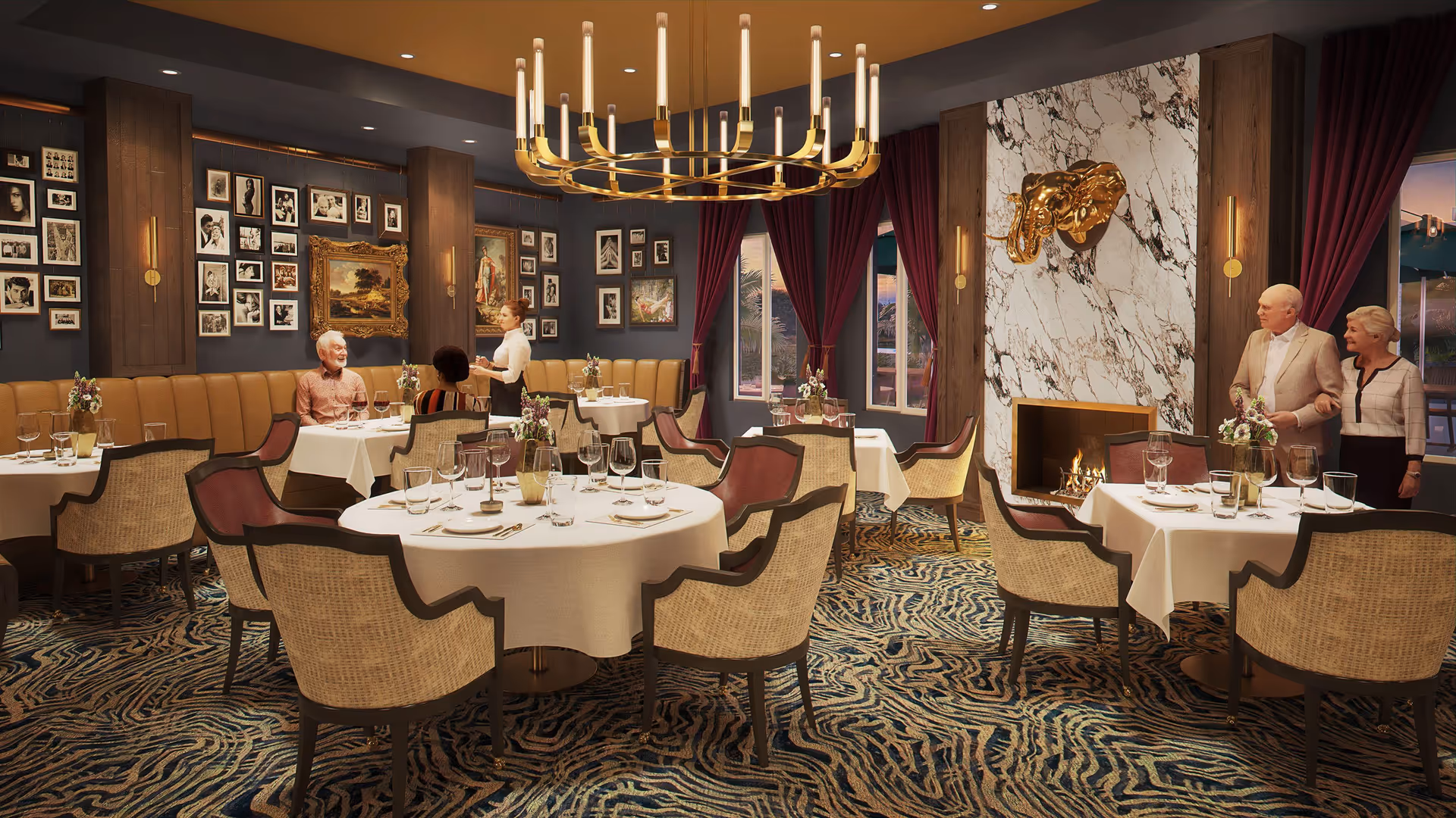 Elegant dining room with round tables covered in white tablecloths, set with glassware and floral centerpieces. Several upholstered chairs surround the tables. The room features a large modern chandelier, a marble fireplace with a golden elephant head sculpture above it, dark walls adorned with numerous framed pictures, and large windows with burgundy curtains. Two elderly couples and a waitress are present in the room.