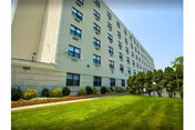 Low-angle exterior view of a multi-story residential care building with rows of windows, a green lawn, and shrubs.