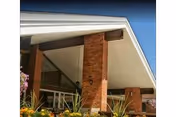 Entrance canopy of a brick building with large angled roof, columns and landscaping in front.