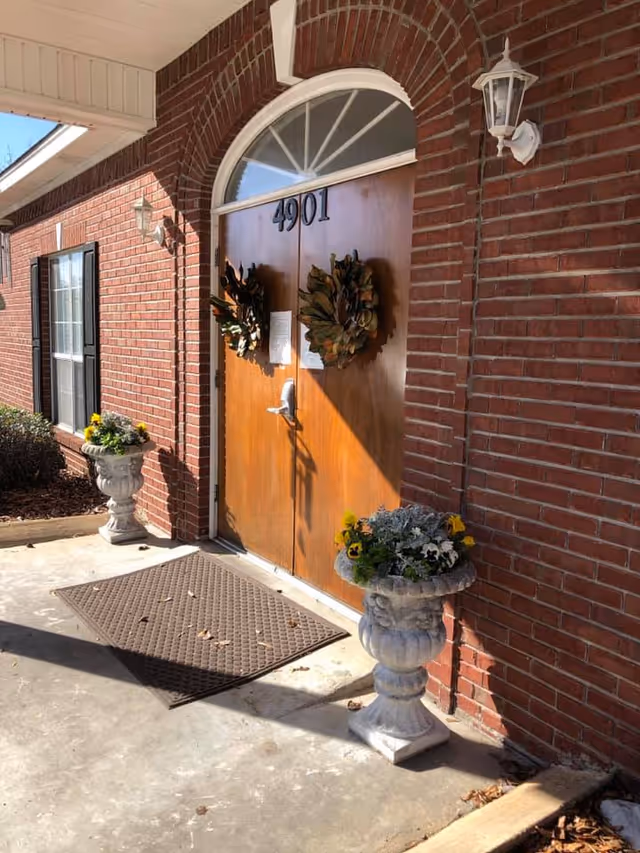 Red brick building entrance with double wooden doors numbered 4901, wreaths on the doors and floral urns on either side.