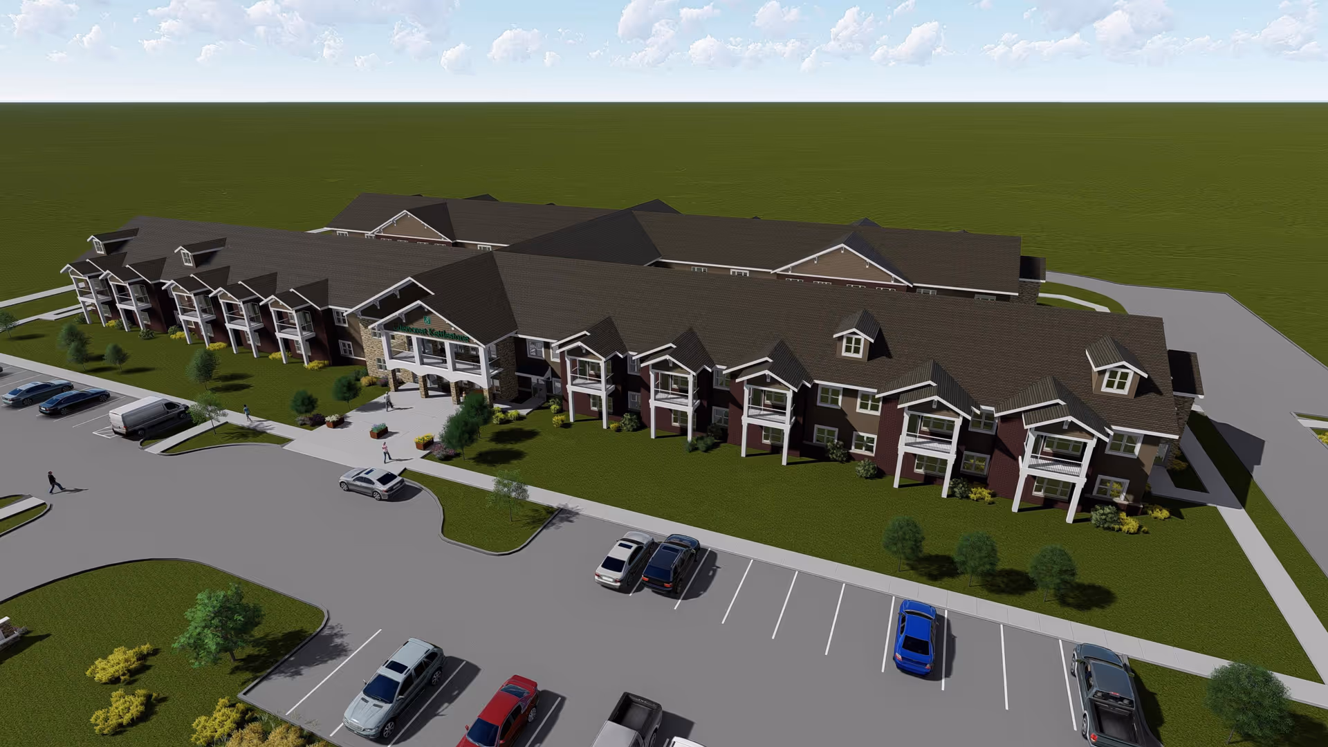 Aerial view of a large two-story senior living facility building with covered entrances, balconies, landscaped grounds and a parking lot.