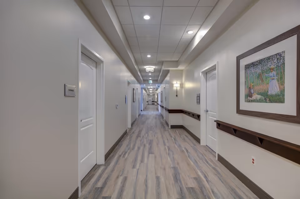 Long, well-lit interior hallway with doors, handrails, artwork, and wood-look flooring.