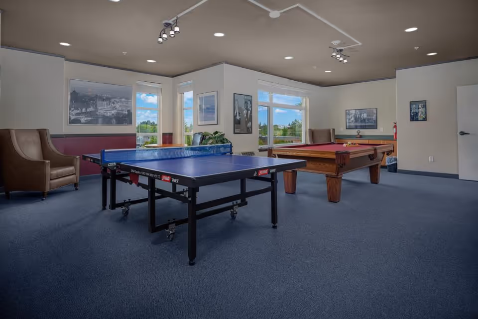 Game room with a ping pong table and a pool table, seating, and windows overlooking greenery.