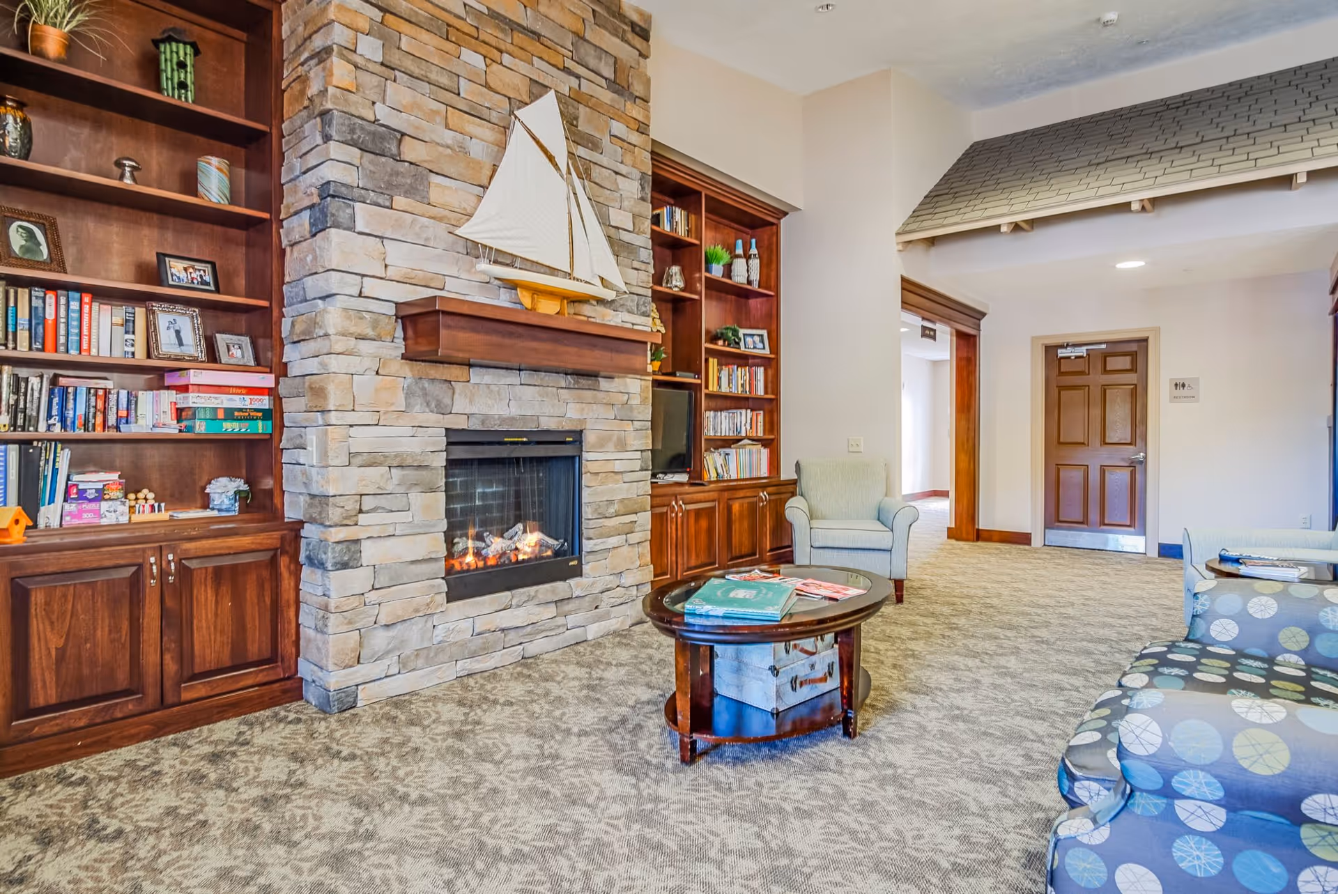 Cozy common room with a stone fireplace, built-in bookshelves, seating and a coffee table.