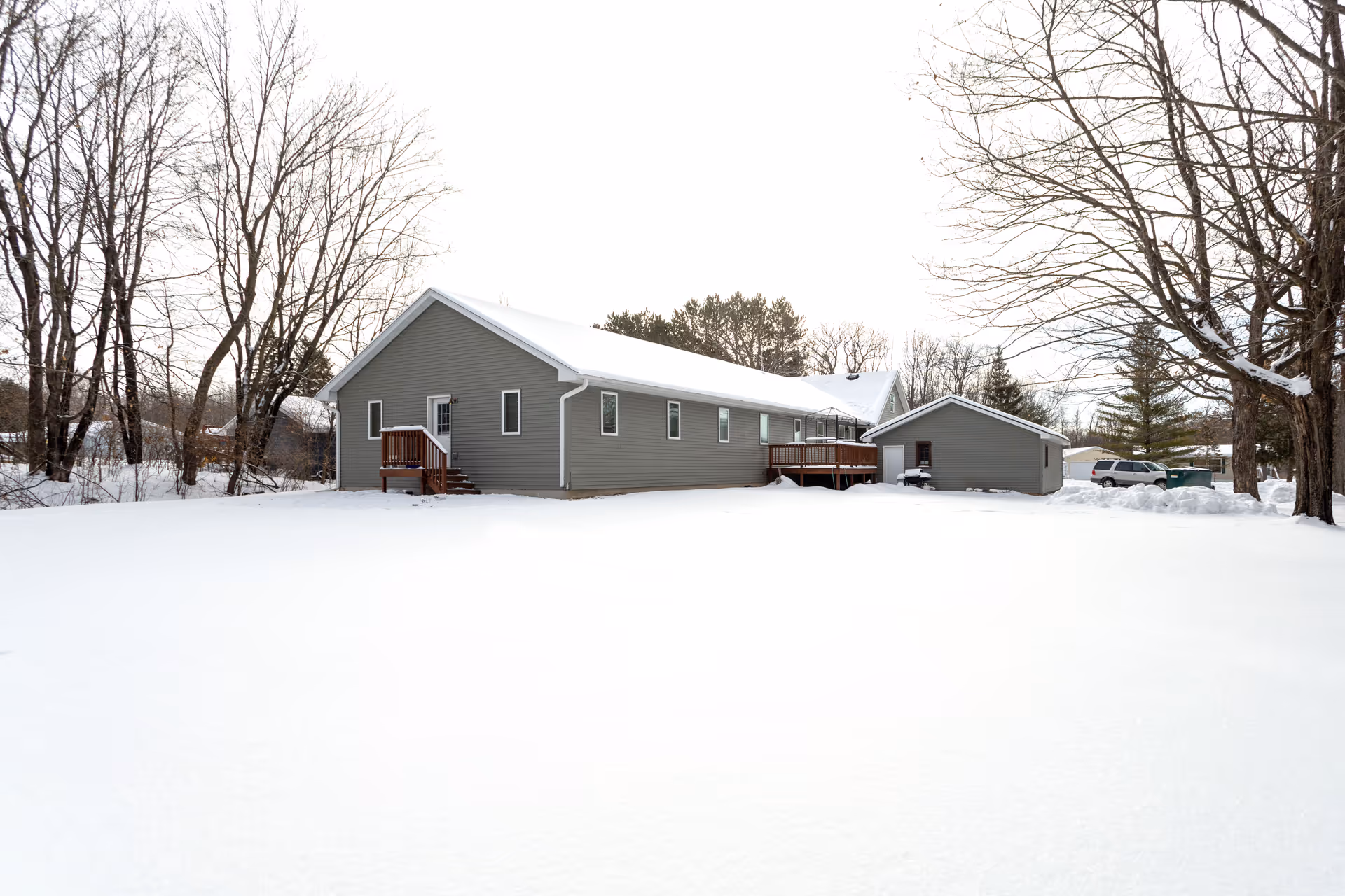 A single-story gray building with white trim surrounded by snow-covered ground and leafless trees under an overcast sky.