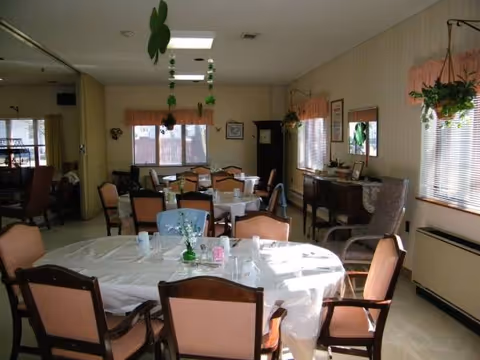 Senior living dining room with round tables, pink chairs, large windows, and hanging greenery.