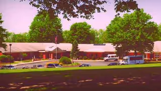 WeCare Sycamore senior living facility front shows a low building with a parking lot and trees.