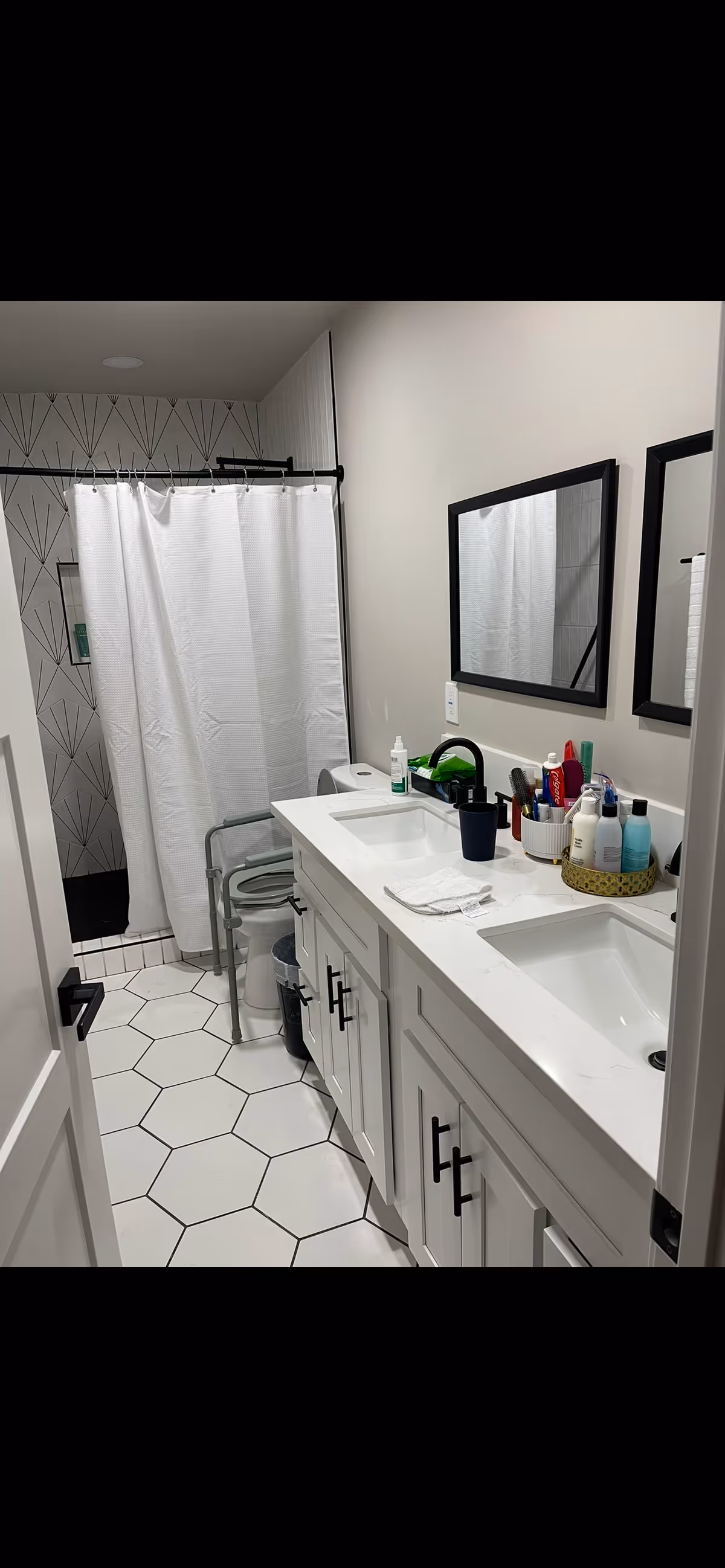 Accessible bathroom with a double-sink white vanity, mirrors, toiletries, and a shower with a white curtain.