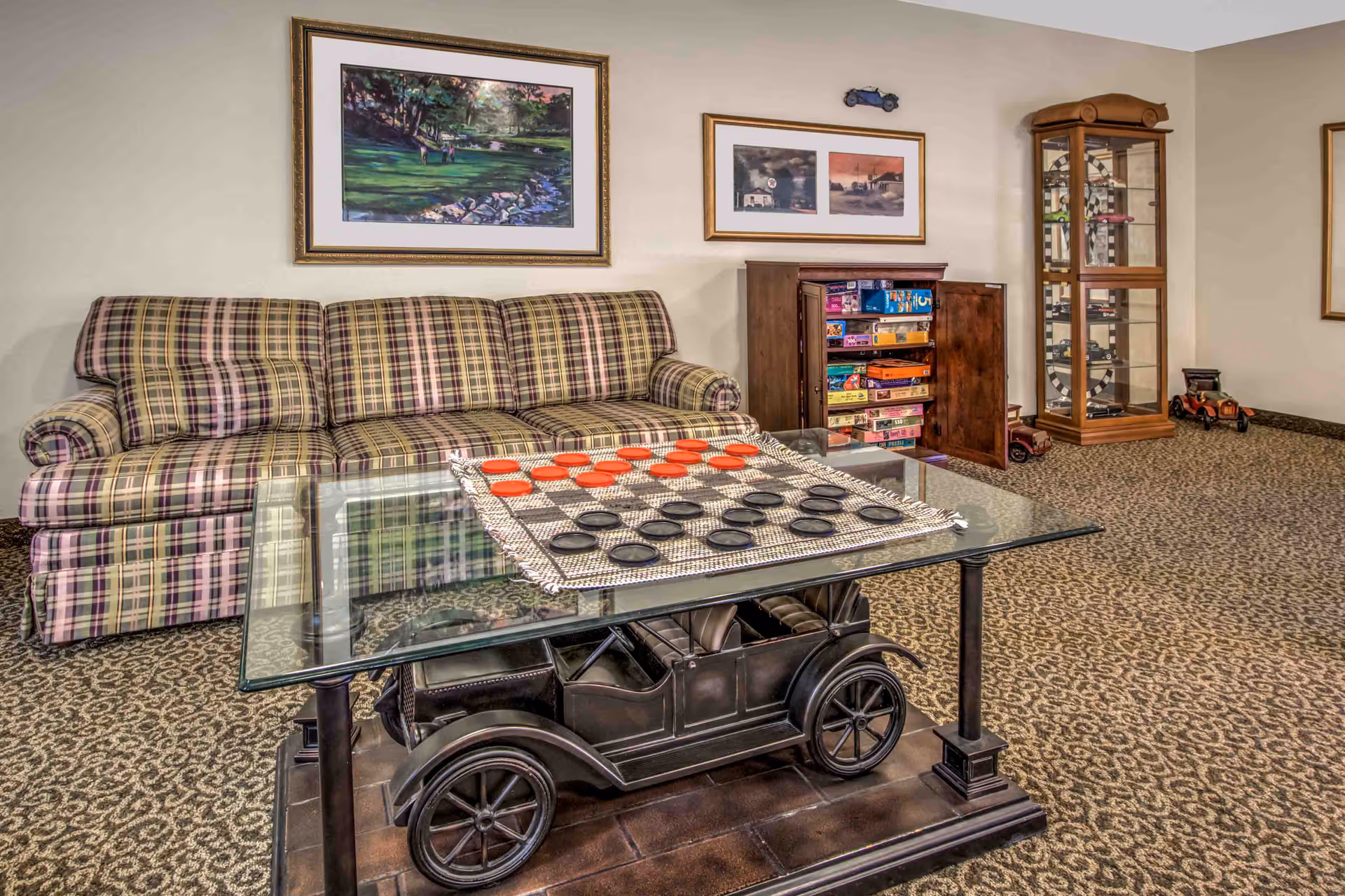 Plaid sofa and a glass-topped coffee table with a checkers board in a cozy lounge game room with shelves of board games and framed artwork.
