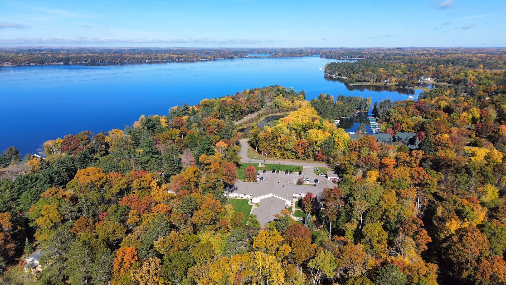 Aerial view of a senior living facility surrounded by colorful autumn trees on the shore of a large lake.