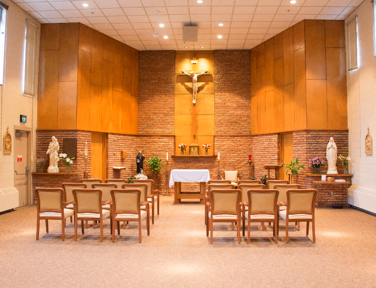 Interior chapel with rows of chairs facing an altar, crucifix, and religious statues.