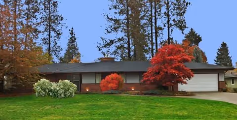 Front view of a single-story house with a driveway, garage, and colorful trees.