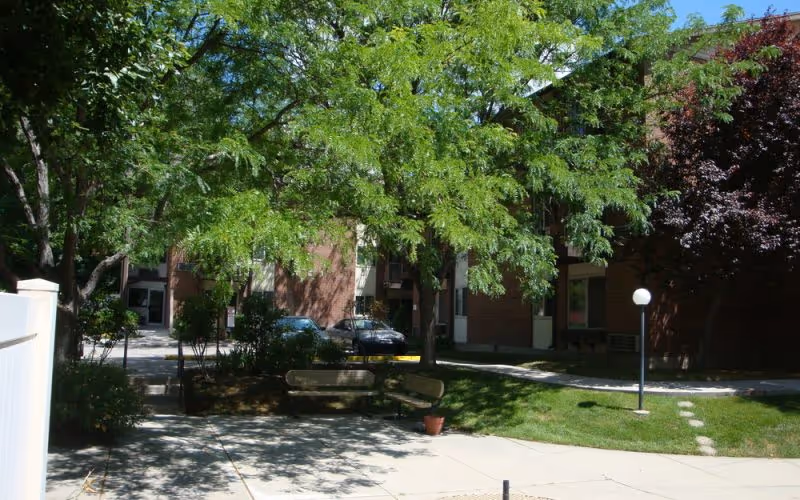 Exterior view of Capitol Villa with brick building, trees, benches, and a paved walkway.