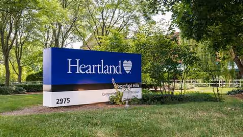 Blue Heartland sign for Bloomfield Hills on a grassy, tree-lined lawn.