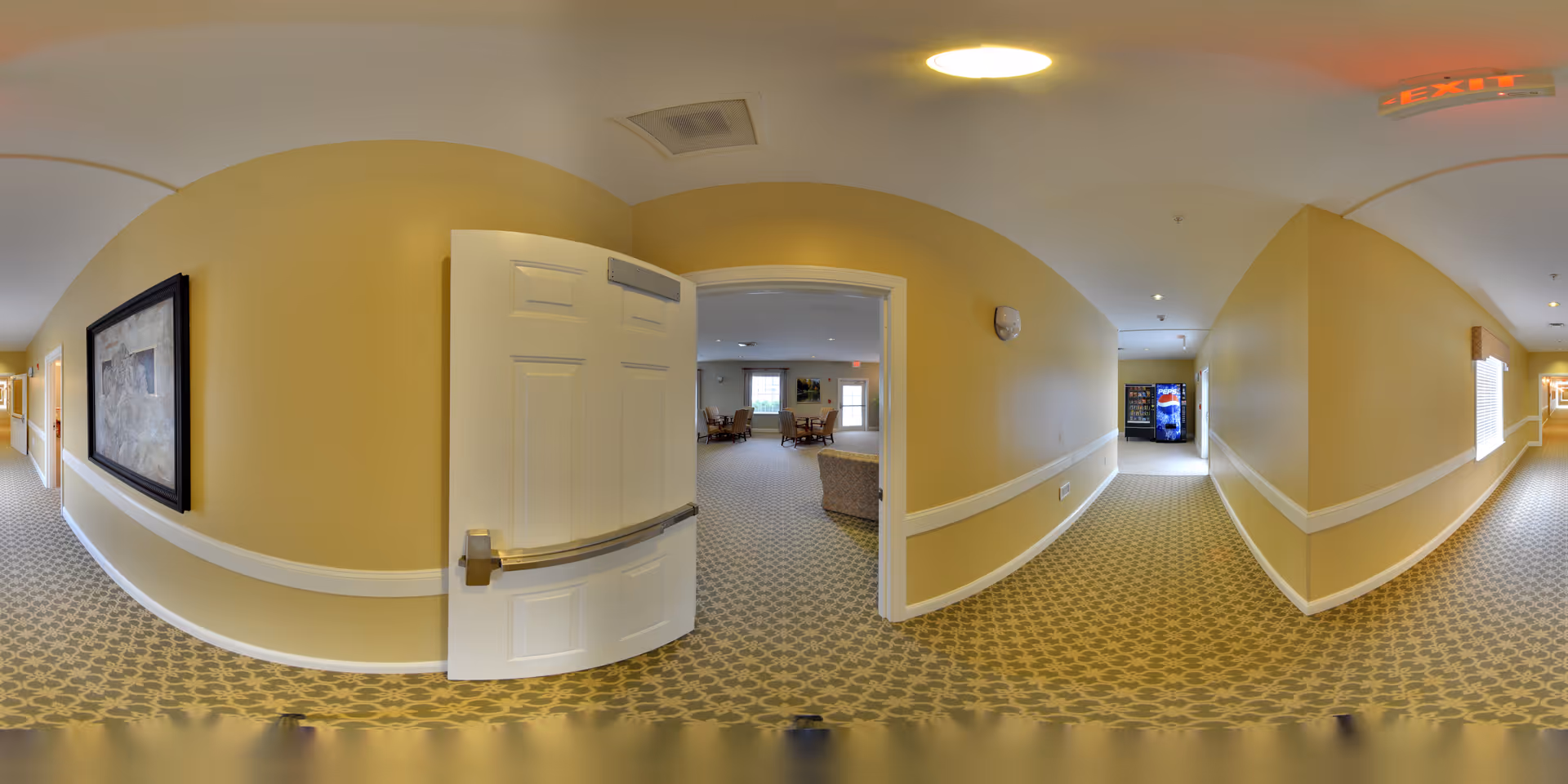 Carpeted interior hallway with yellow walls, a partially open white door into a seating area, and a vending machine visible at the far end.