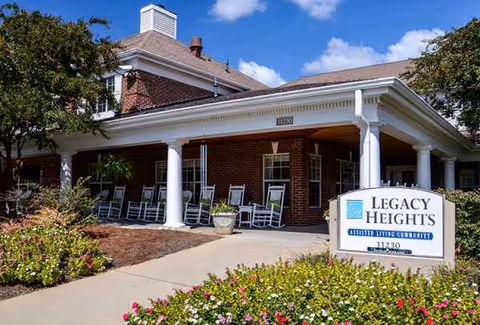 Brick senior living facility exterior with a front porch, rocking chairs, and a sign.