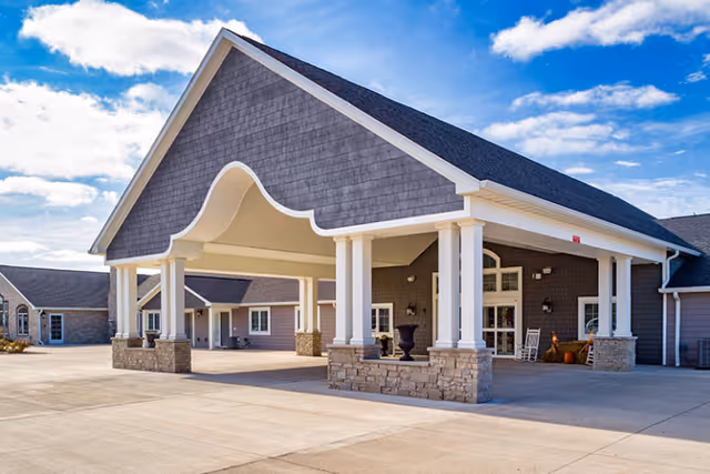 Entrance of a single-story assisted living building with a large covered porte-cochere supported by white columns.