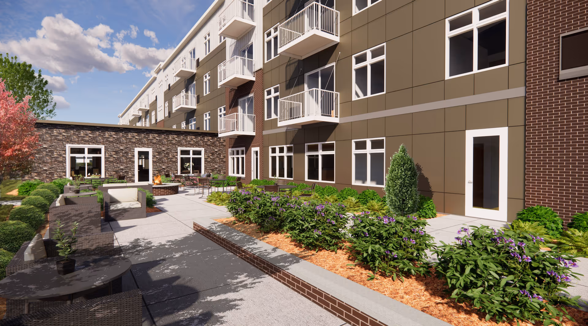 Outdoor patio area of a senior living facility with seating arrangements including chairs and tables, surrounded by landscaped greenery and flowers. The building has multiple floors with balconies and large windows. The sky is partly cloudy.