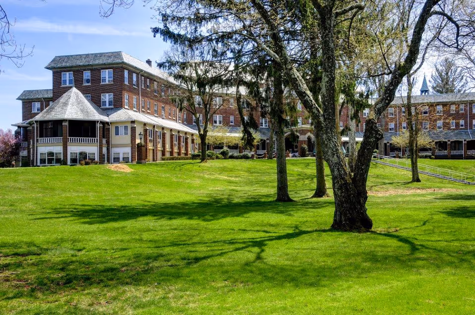 Large brick multi-story residential building set behind a grassy lawn with several trees.