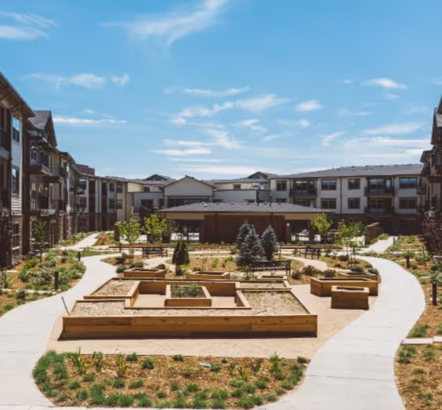 Central landscaped courtyard with raised garden beds, walking paths and surrounding multi-story residential buildings under a blue sky.