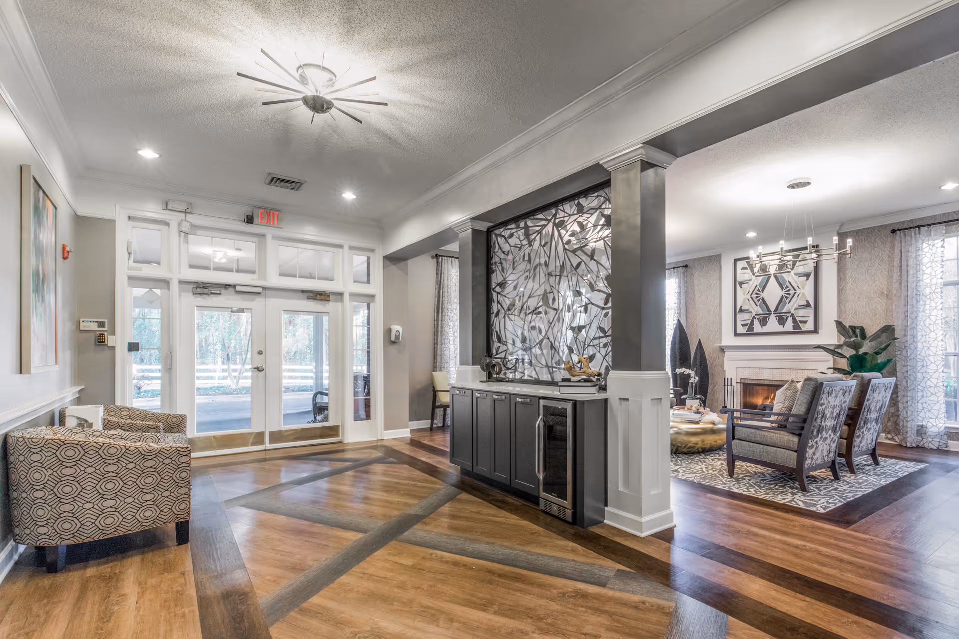 Spacious, well-lit senior living facility lobby with seating area, decorative divider, wood floors and glass double doors.