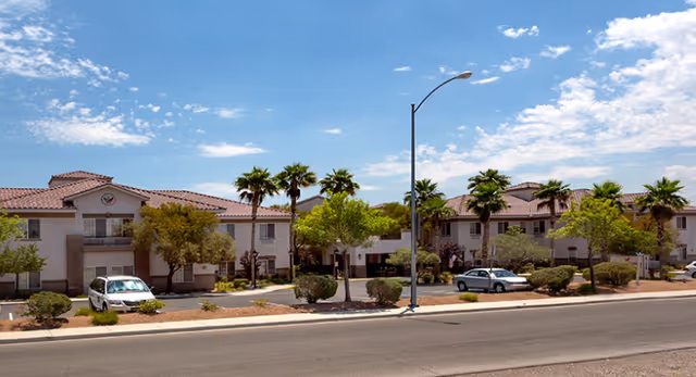 Exterior view of Heritage Springs Assisted Living and Memory Care building with palm trees, parked cars.