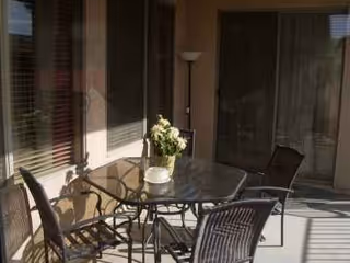 Outdoor patio with glass table, metal chairs, and a potted plant near sliding doors.