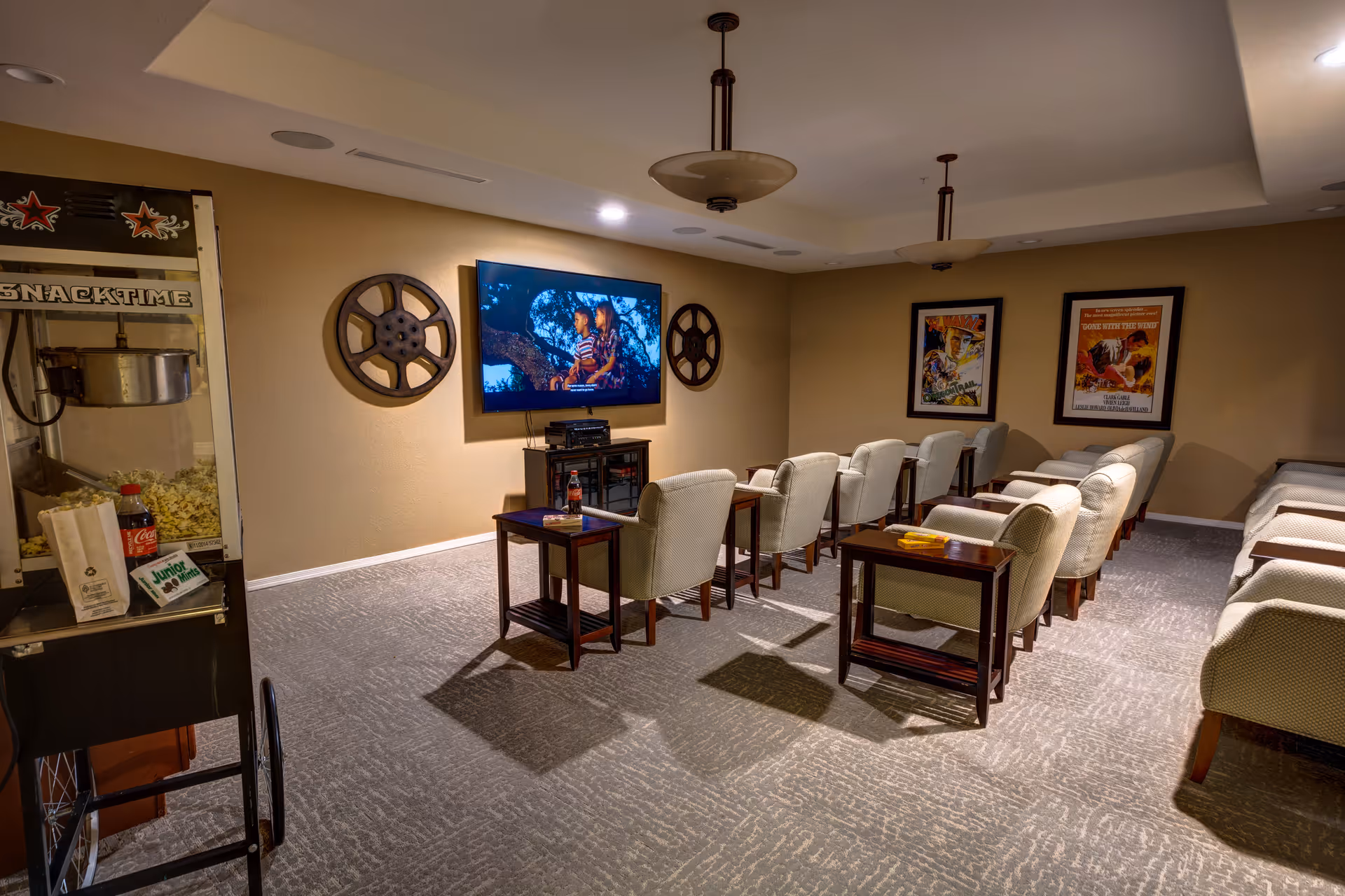 Cozy screening room with rows of armchairs facing a wall-mounted TV, side tables, framed movie posters, and a popcorn machine.