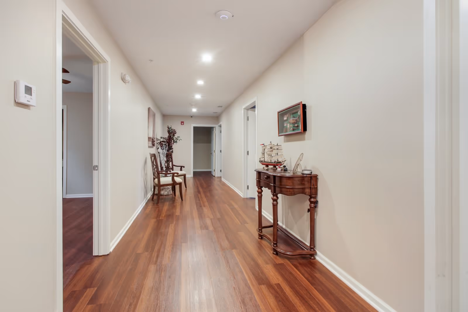 Well-lit interior hallway with wood floors, chairs and a decorative console table against the wall.
