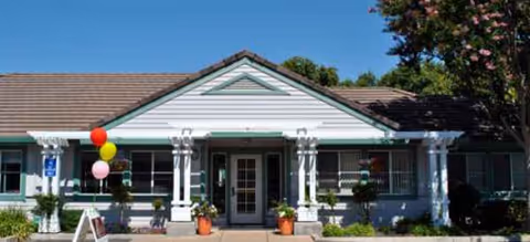 Front view of a single-story senior living facility with a covered entrance and balloons.