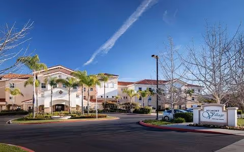 Wide view of Belmont Village Senior Living Sabre Springs exterior, with palm trees and circular driveway.