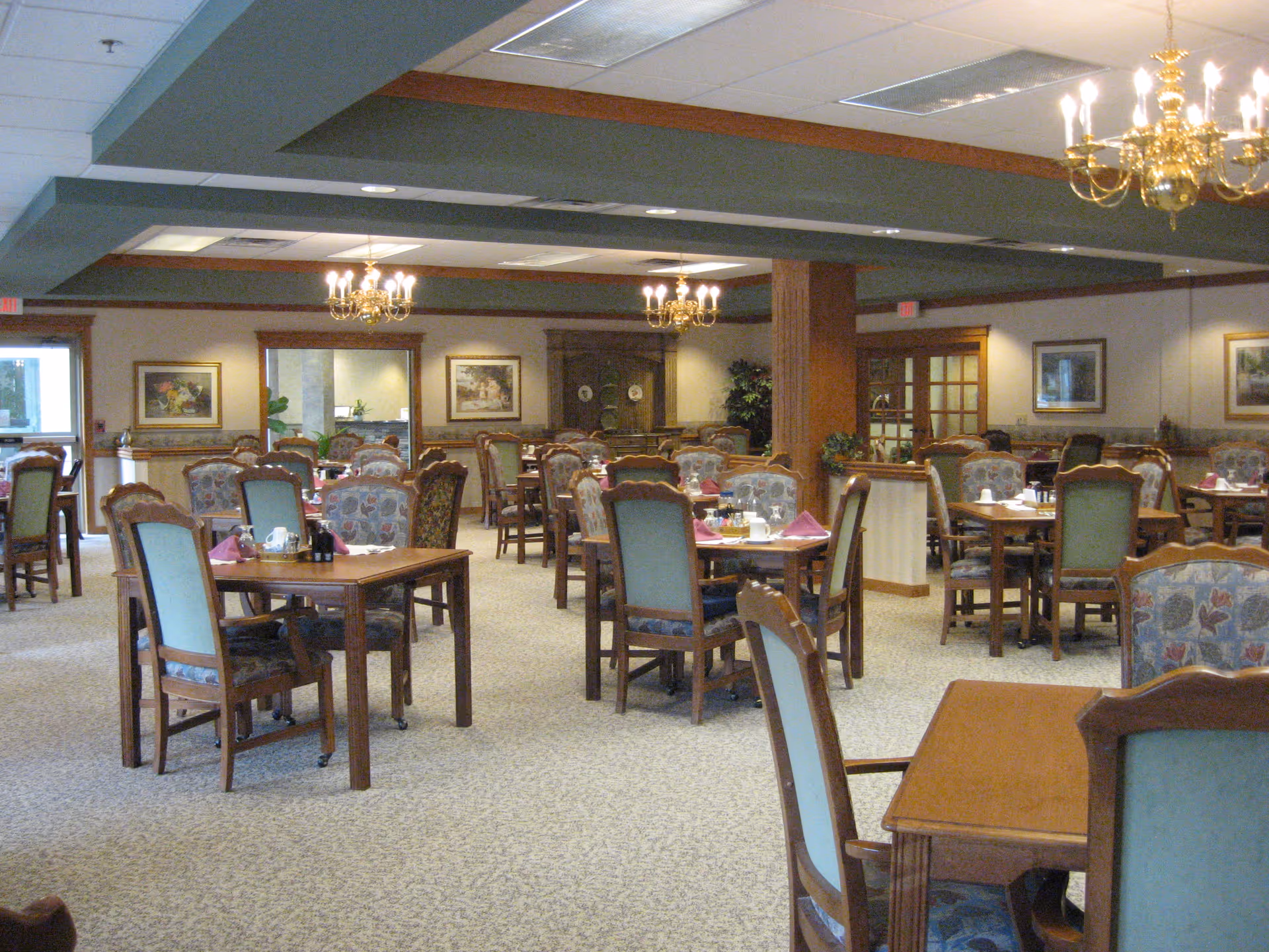 Spacious dining room with multiple wooden tables and upholstered chairs set under chandeliers.