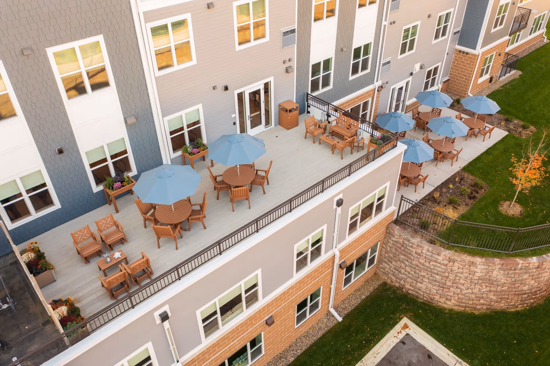Aerial view of an outdoor terrace with round tables, blue umbrellas, and wooden seating alongside the building.