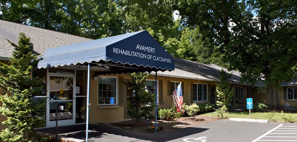 Front entrance of Avamere Rehabilitation of Clackamas with a blue awning, American flag, and accessible parking spaces.