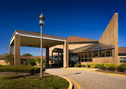 Brick entrance of a senior living facility with a covered drop-off area and lamp.