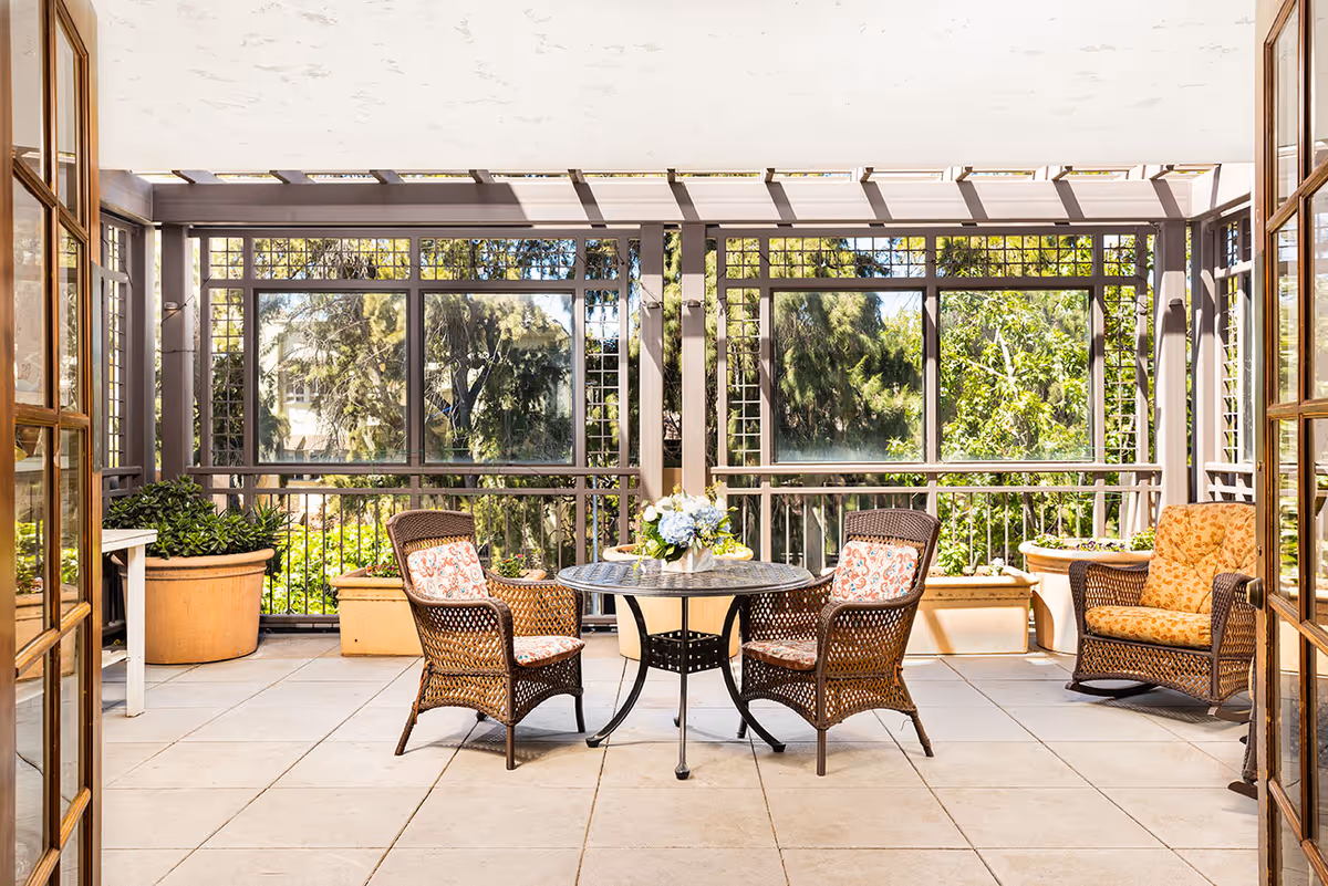 Sunlit screened patio with wicker chairs and a round table overlooking trees.