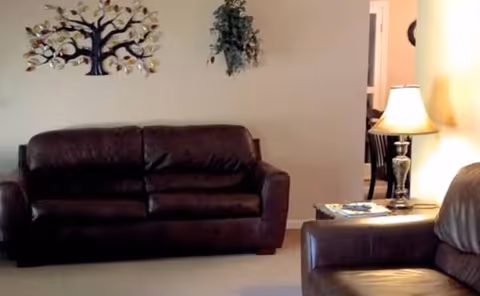 Dark brown leather sofa and chair set in a living room with wall art and lamp.