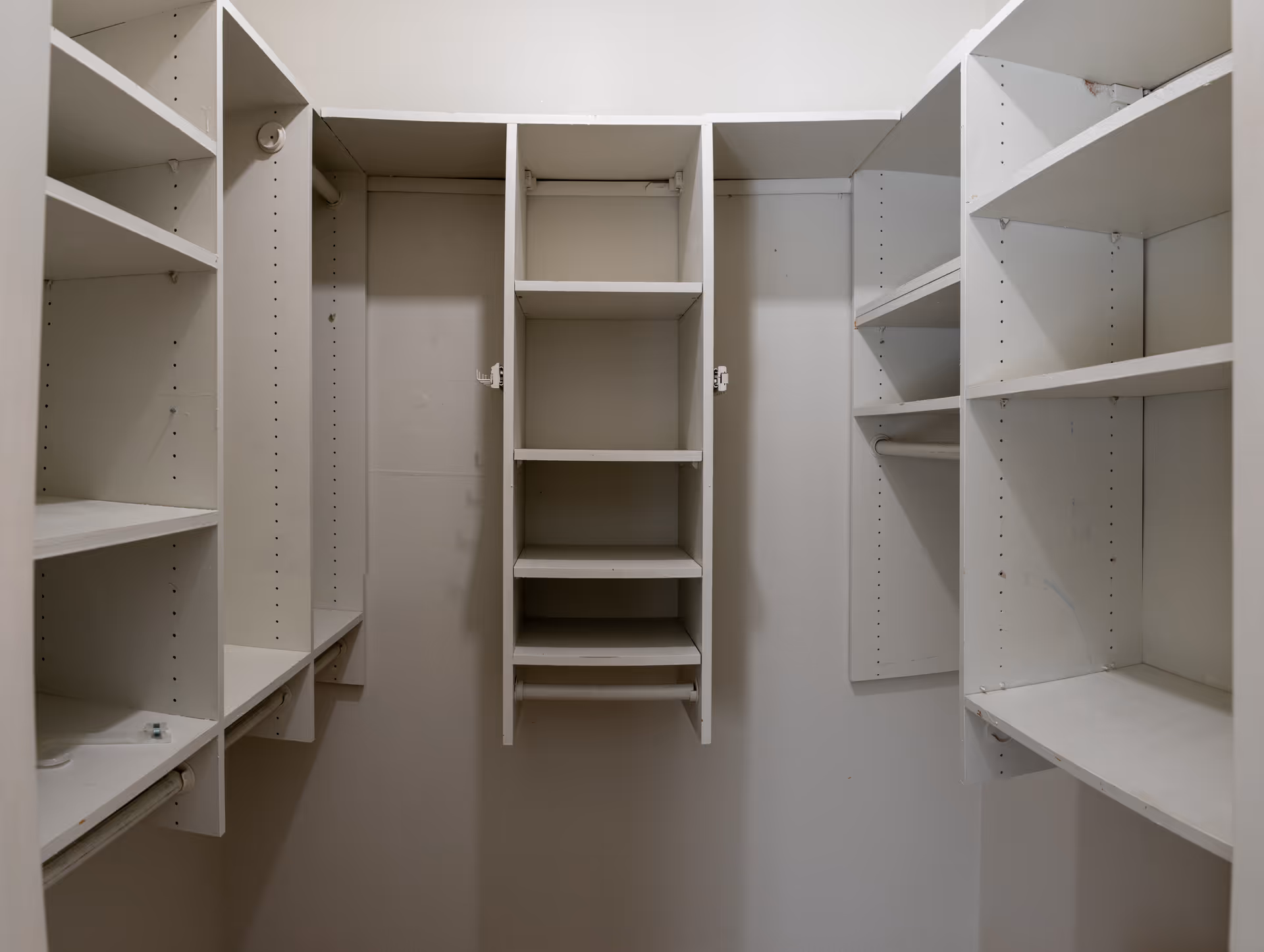 Empty walk-in closet with white built-in shelves and hanging rods on three walls.