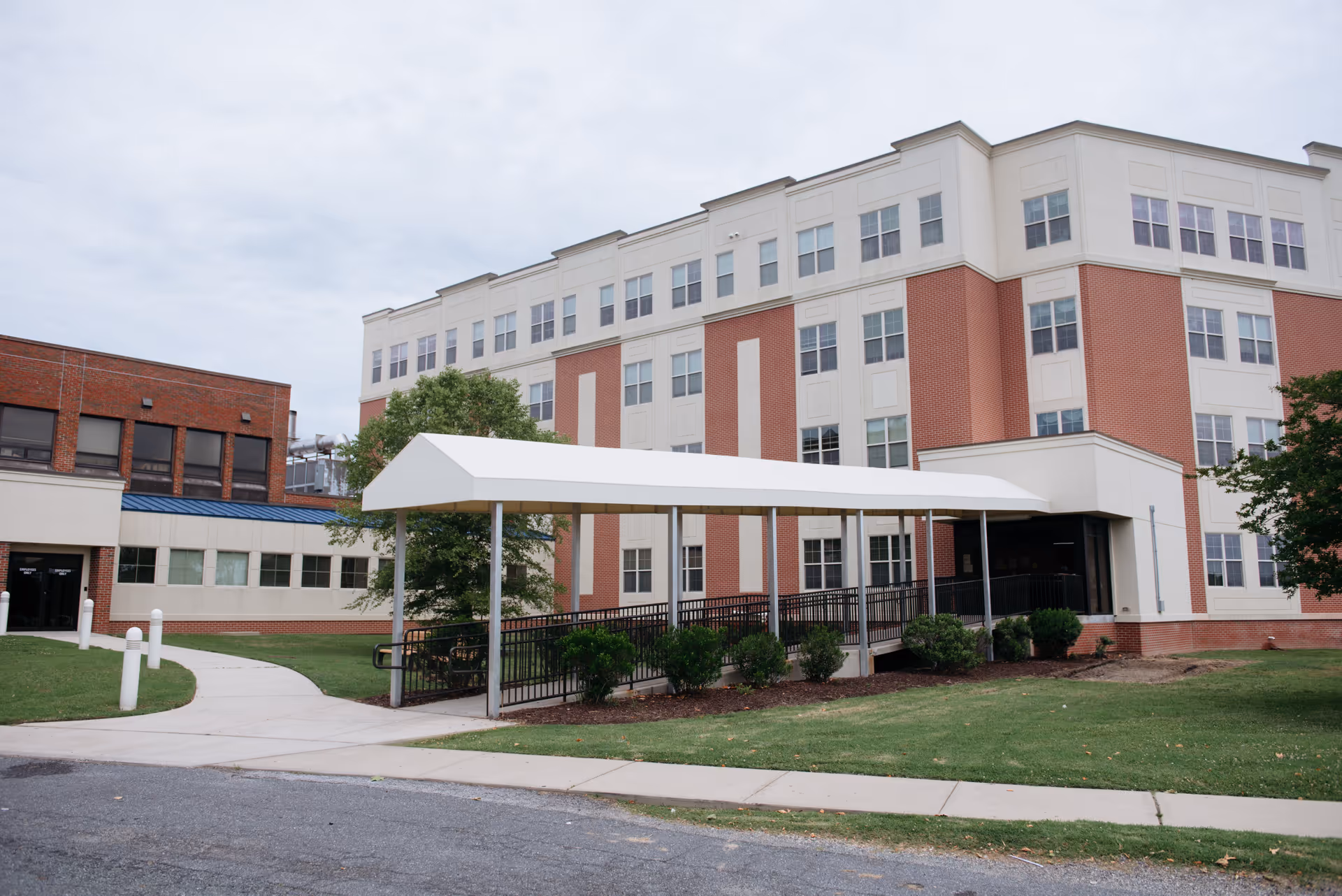 Multi-story brick-and-white senior living building with a covered entrance ramp and surrounding lawn.