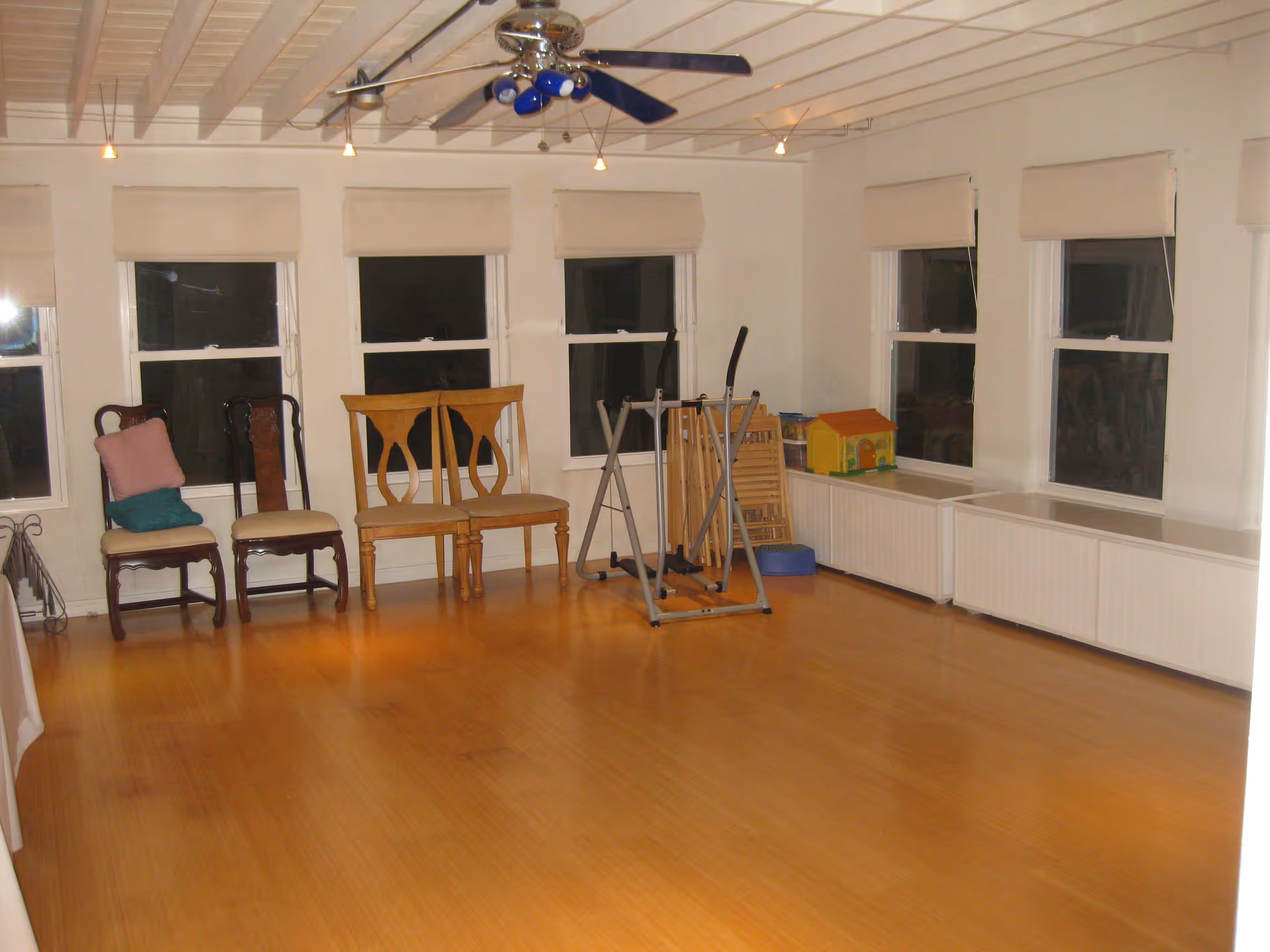 Large multipurpose interior room with a wooden floor, row of windows, several chairs along the wall and an exercise machine.