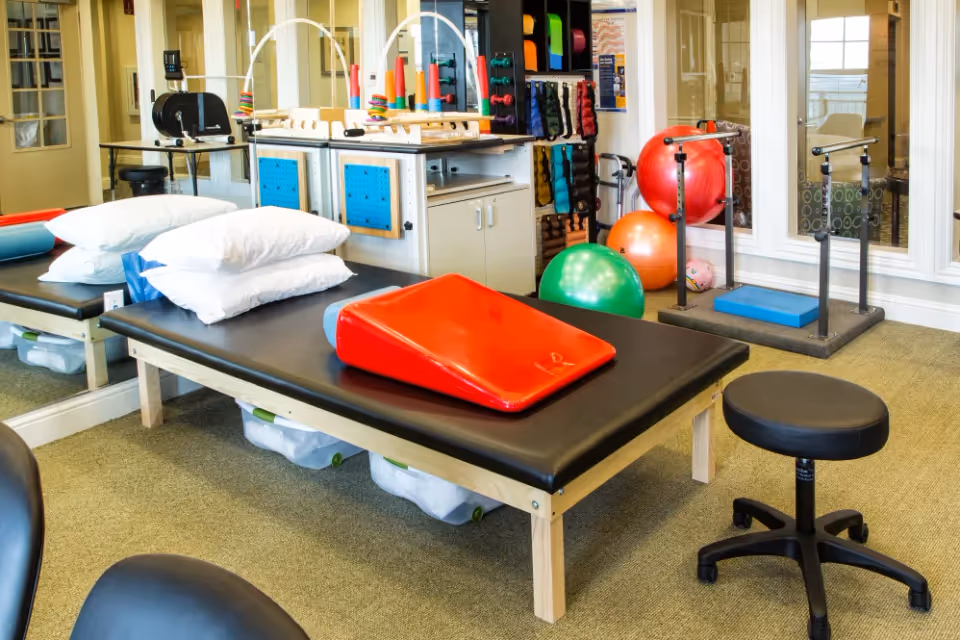 Physical therapy room with a treatment table, pillows, exercise balls, and various therapy equipment.