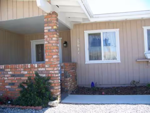 Front porch of a beige senior living facility with brick columns and a window.