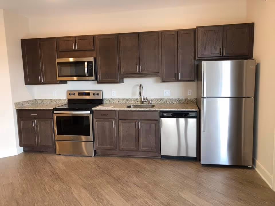 Kitchen with stainless steel refrigerator, oven, microwave, dishwasher, granite countertop, and dark wood cabinets.