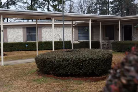 Exterior view of a single-story senior living building with hedges and a covered walkway.