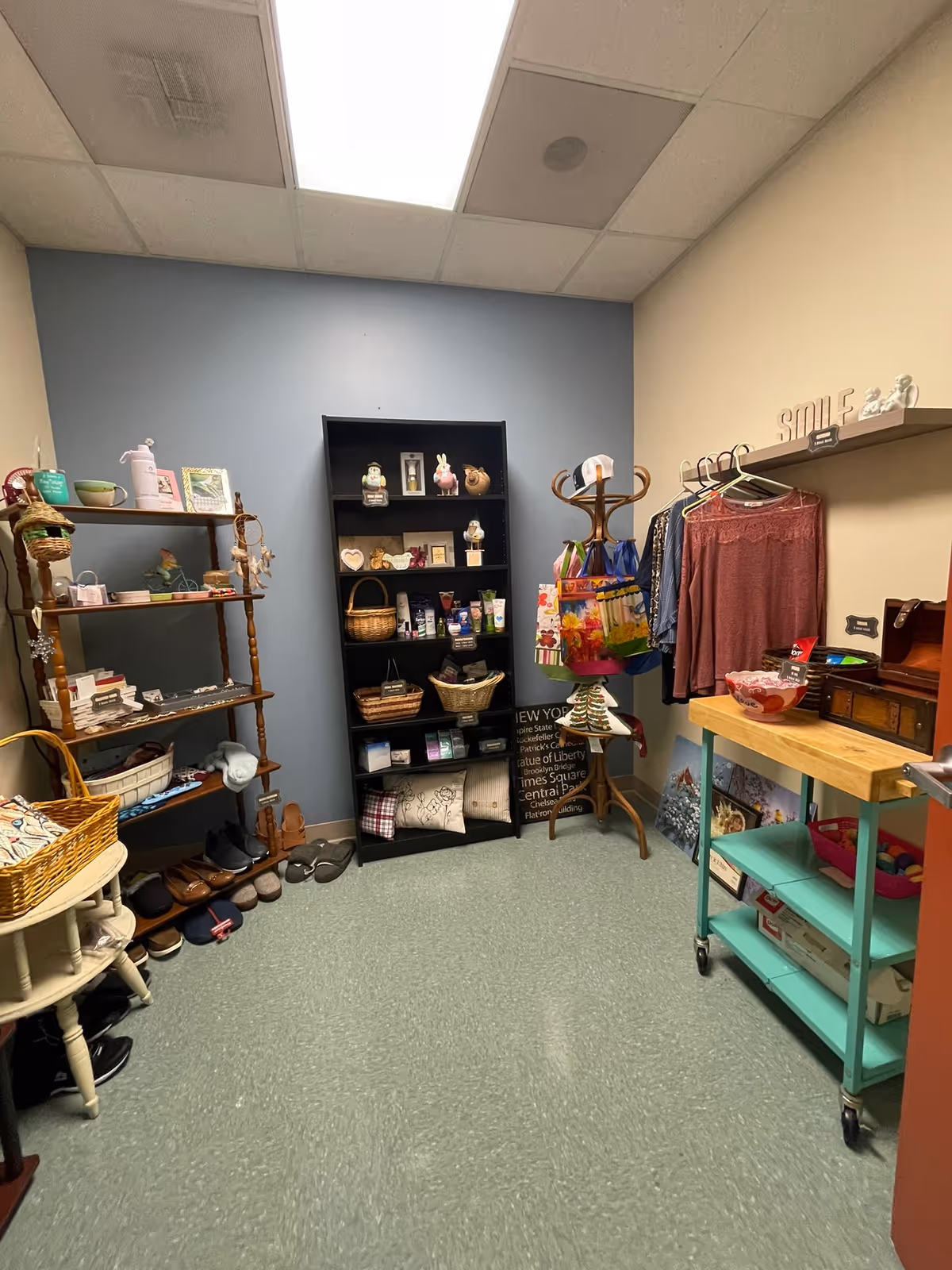 Small interior boutique-style room with shelves, baskets, shoes and a clothing rack displaying garments and gifts.