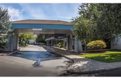 Exterior view of Evergreen Estates facility entrance with a covered driveway, surrounded by trees and greenery under a partly cloudy sky.