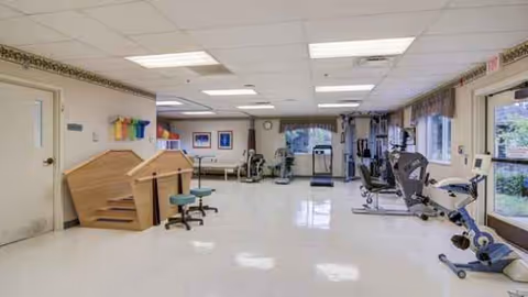Bright indoor rehabilitation gym with exercise machines and therapy equipment.